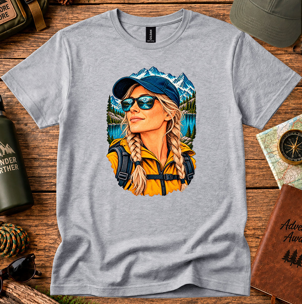 Grey T-shirt featuring a woman wearing a blue cap and sunglasses with mountain and lake scenery