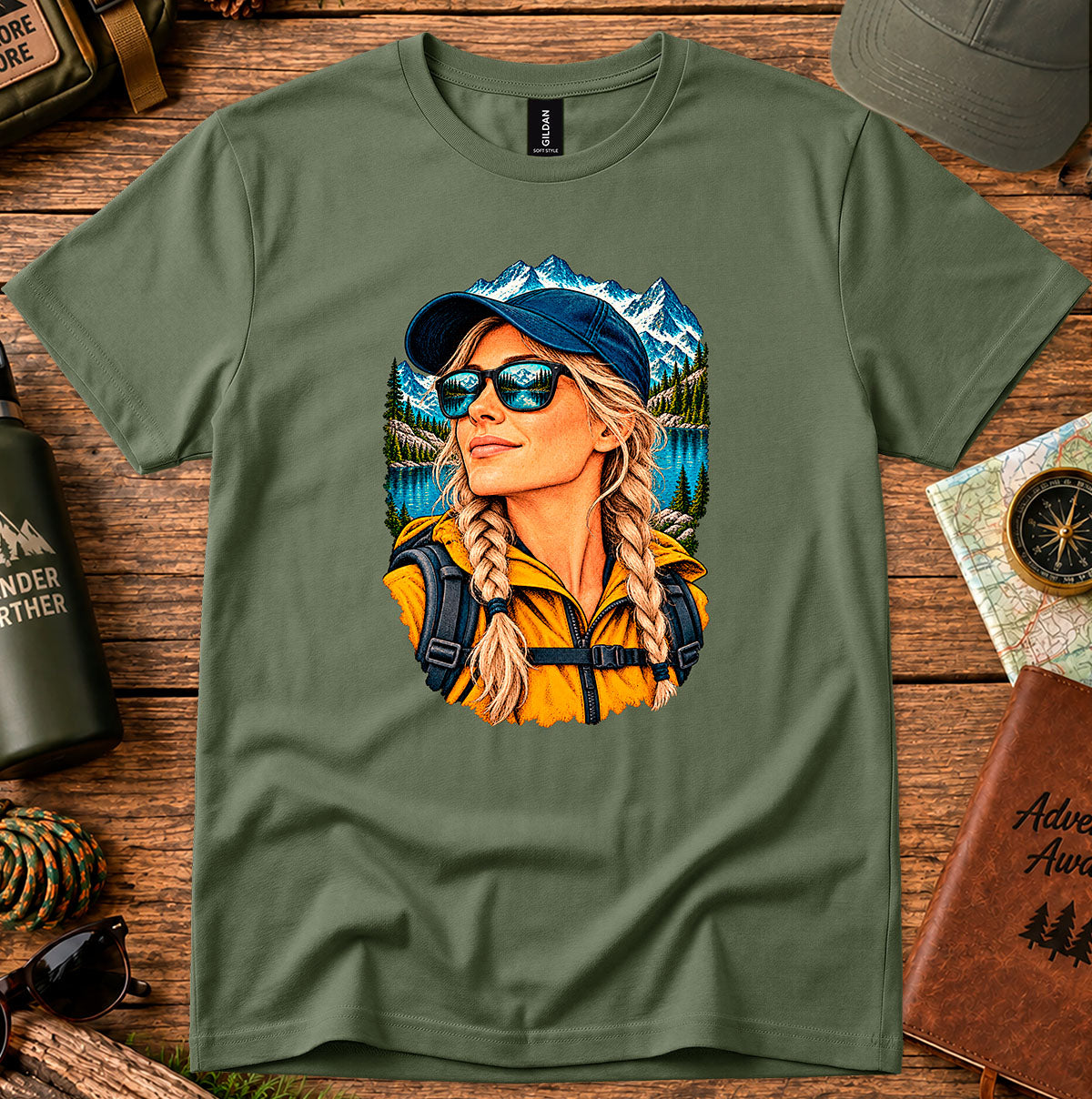 Olive green T-shirt featuring a woman wearing a blue cap and sunglasses with mountain and lake scenery
