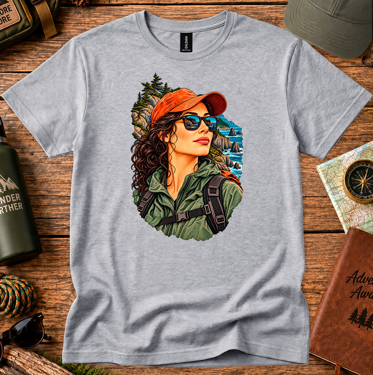 Grey T-shirt featuring a woman in a red cap and sunglasses surrounded by mountain and forest scenery