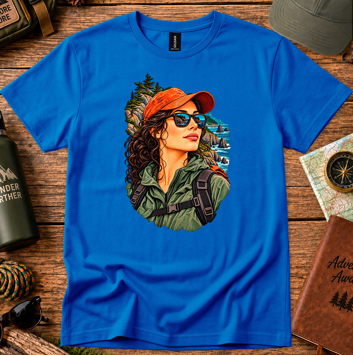 Royal blue T-shirt featuring a woman in a red cap and sunglasses surrounded by mountain and forest scenery