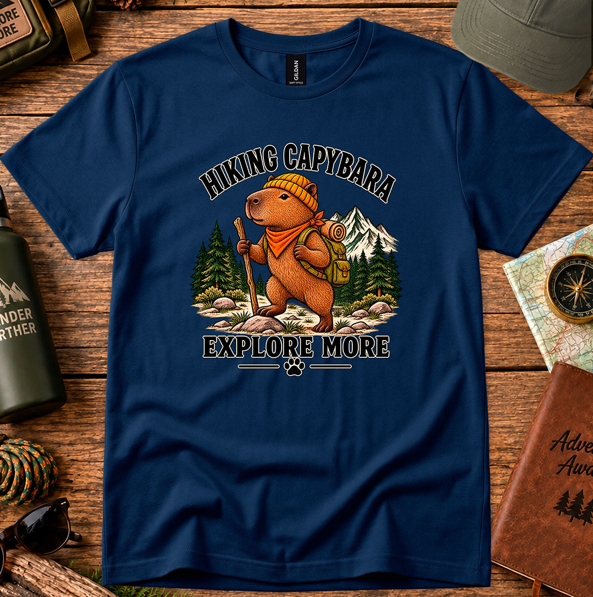 Navy T-shirt featuring a capybara wearing a backpack and bandana, framed by pine trees and mountains