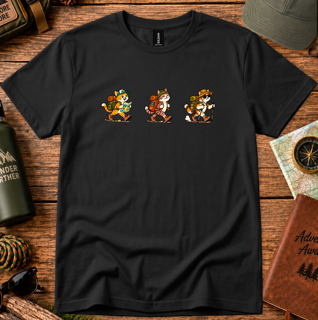 T-shirt featuring three cartoon cats carrying backpacks and hiking gear