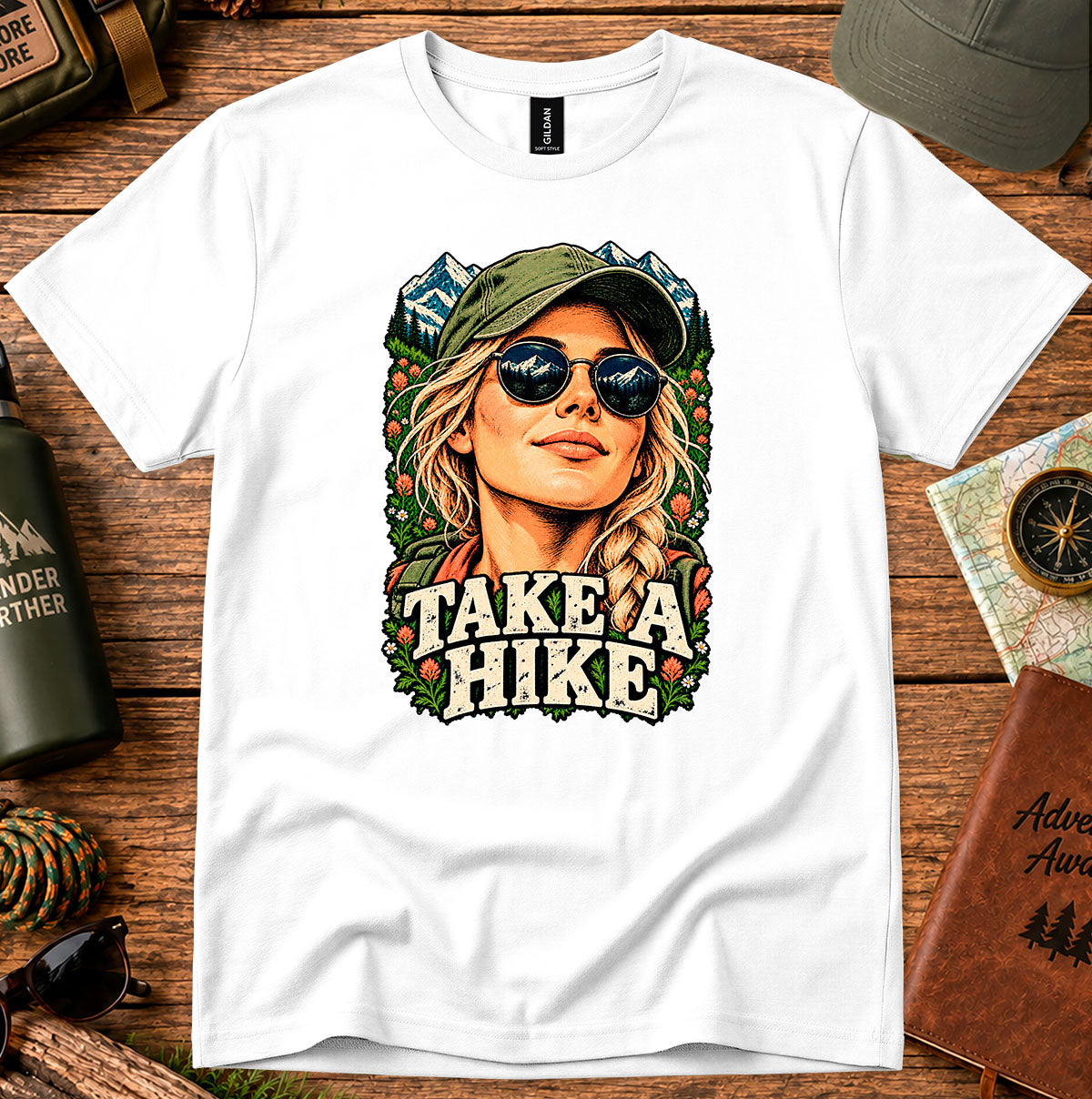 Take a Hike T-shirt showing a woman in a hat framed by mountain peaks and foliage