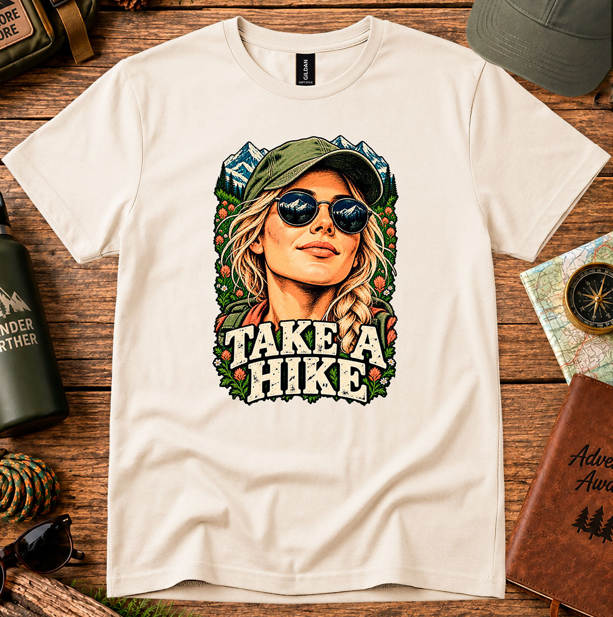 Take a Hike T-shirt showing a woman in a hat framed by mountain peaks and foliage