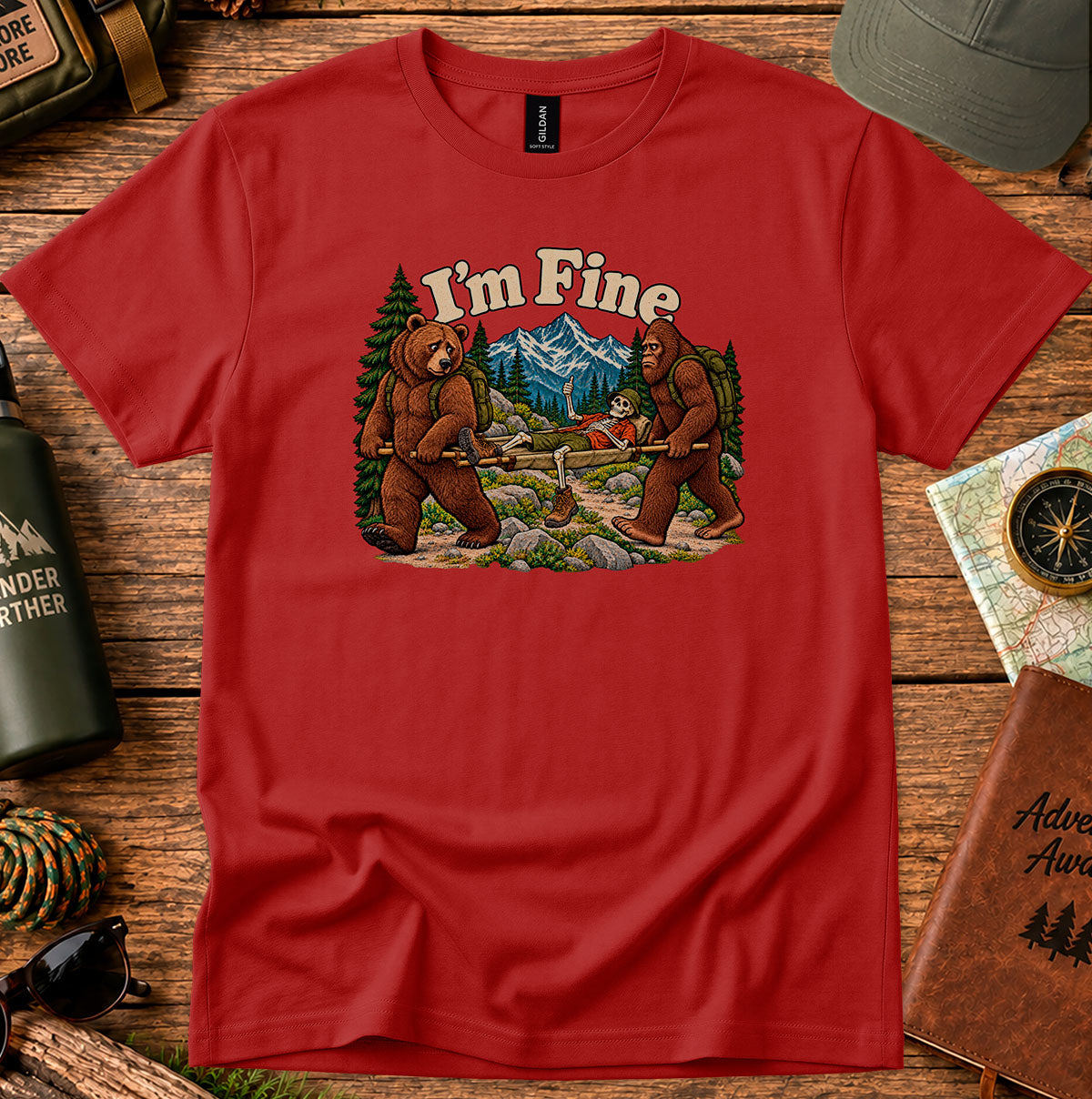 I'm Fine hiking T-shirt with a bear and bigfoot carrying a skeleton on a stretcher among mountains and pine trees