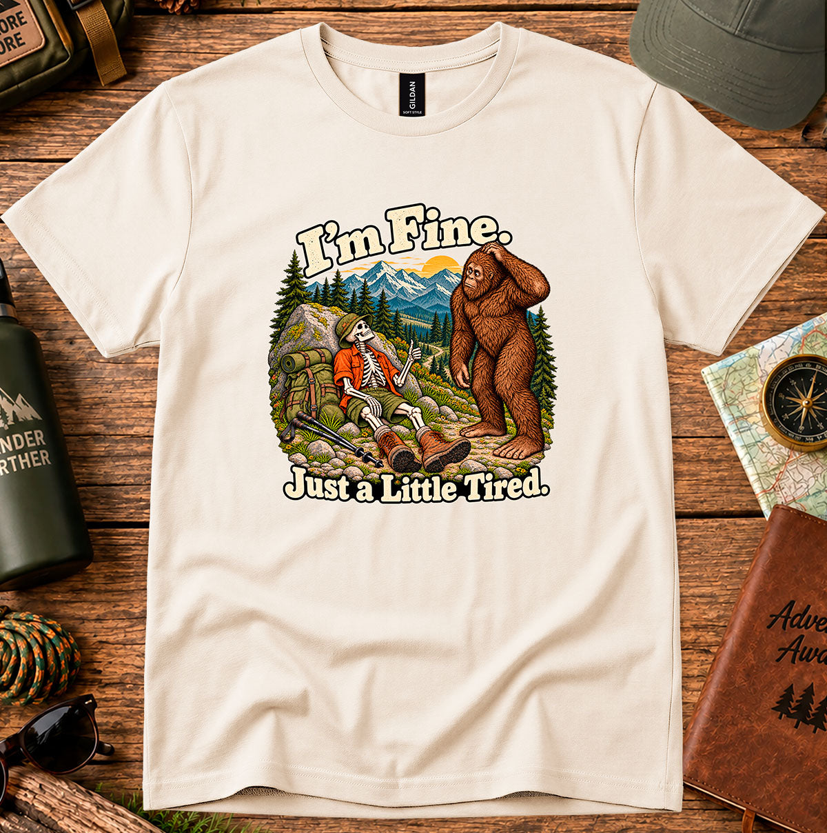 I'm Fine Just a Little Tired T-shirt with a resting skeleton hiker and bigfoot on a mountain trail