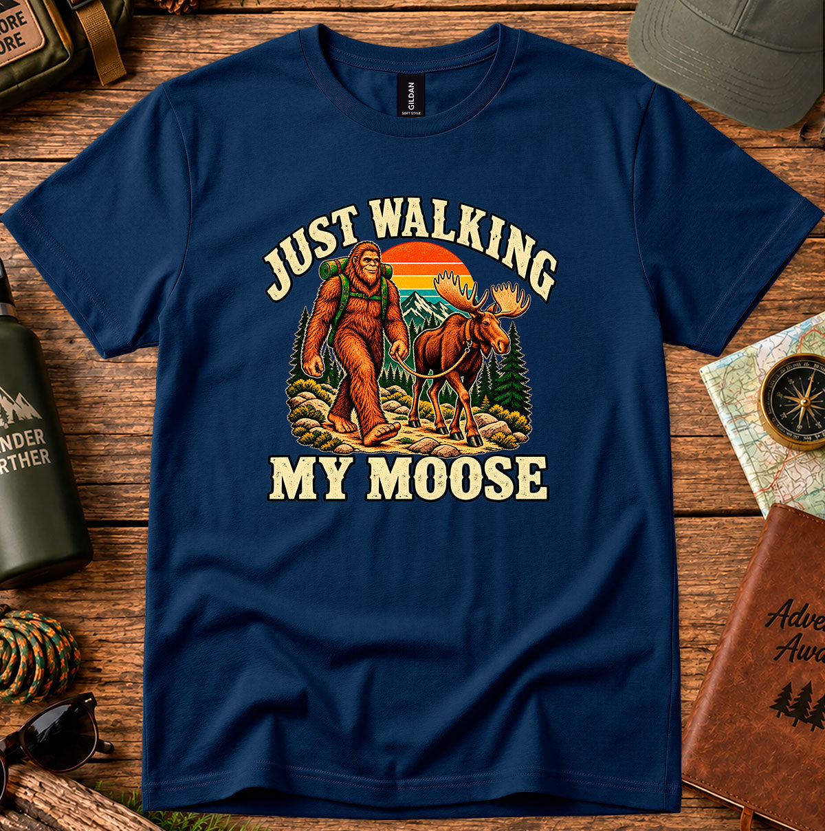 Navy T-shirt featuring Bigfoot walking with a moose through a sunset forest scene