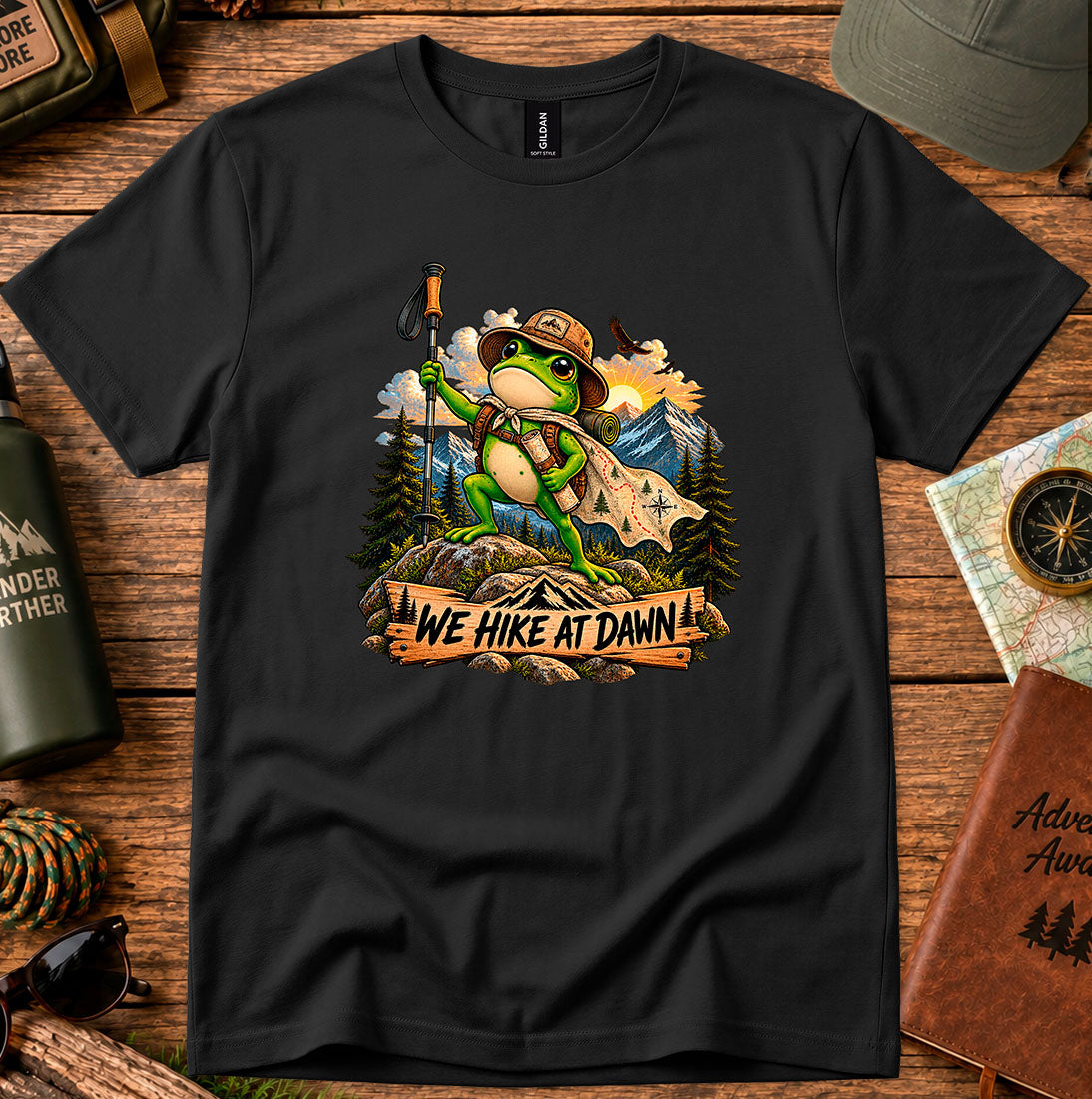 T-shirt featuring a backpack-wearing frog on a rock with mountains and pine trees