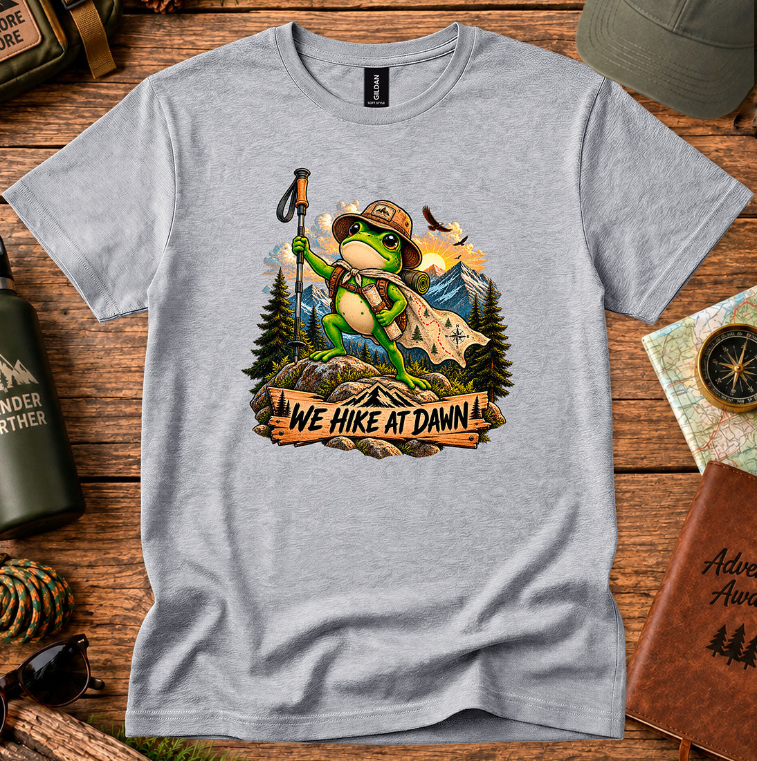 T-shirt featuring a backpack-wearing frog on a rock with mountains and pine trees