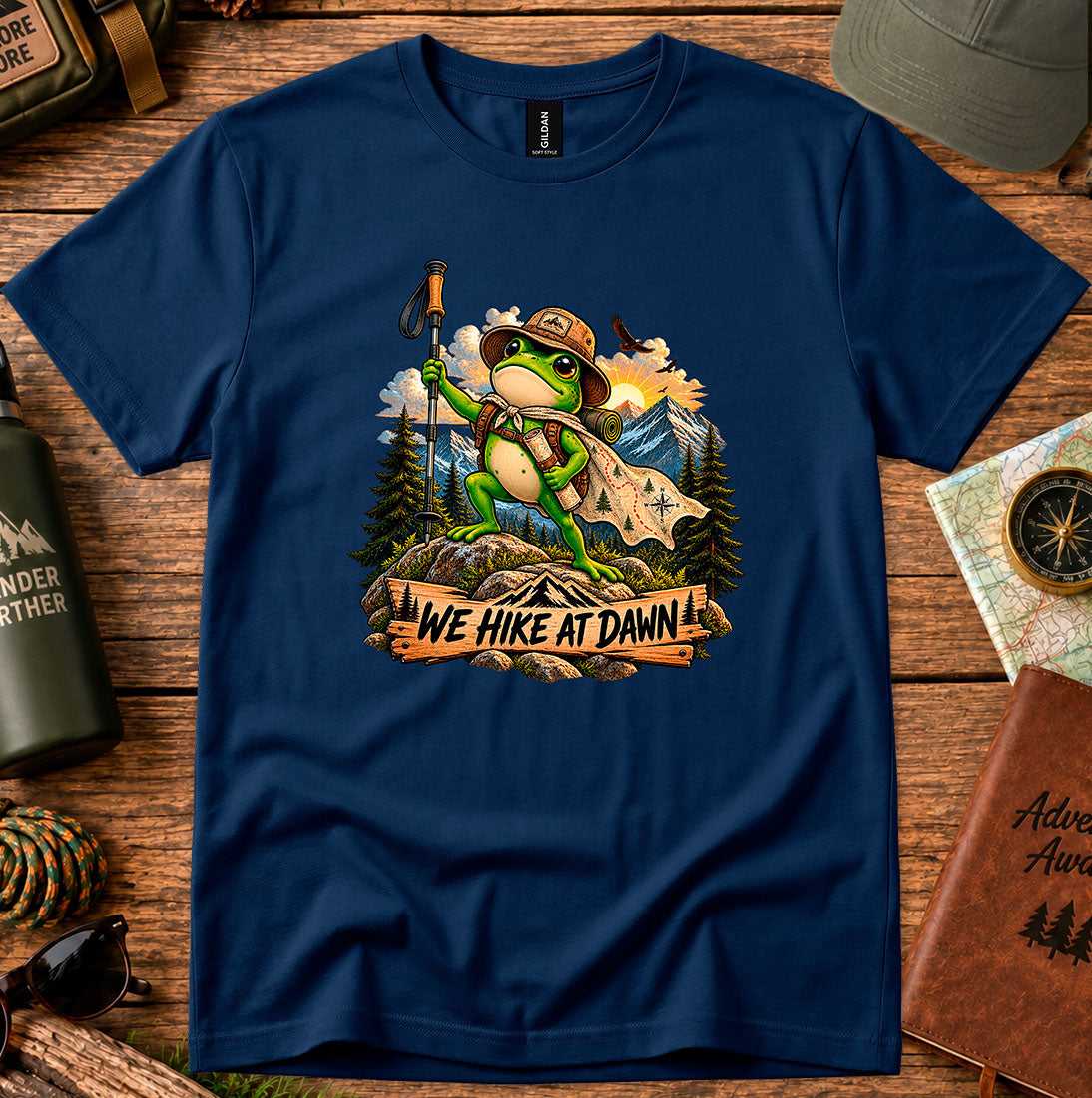 T-shirt featuring a backpack-wearing frog on a rock with mountains and pine trees